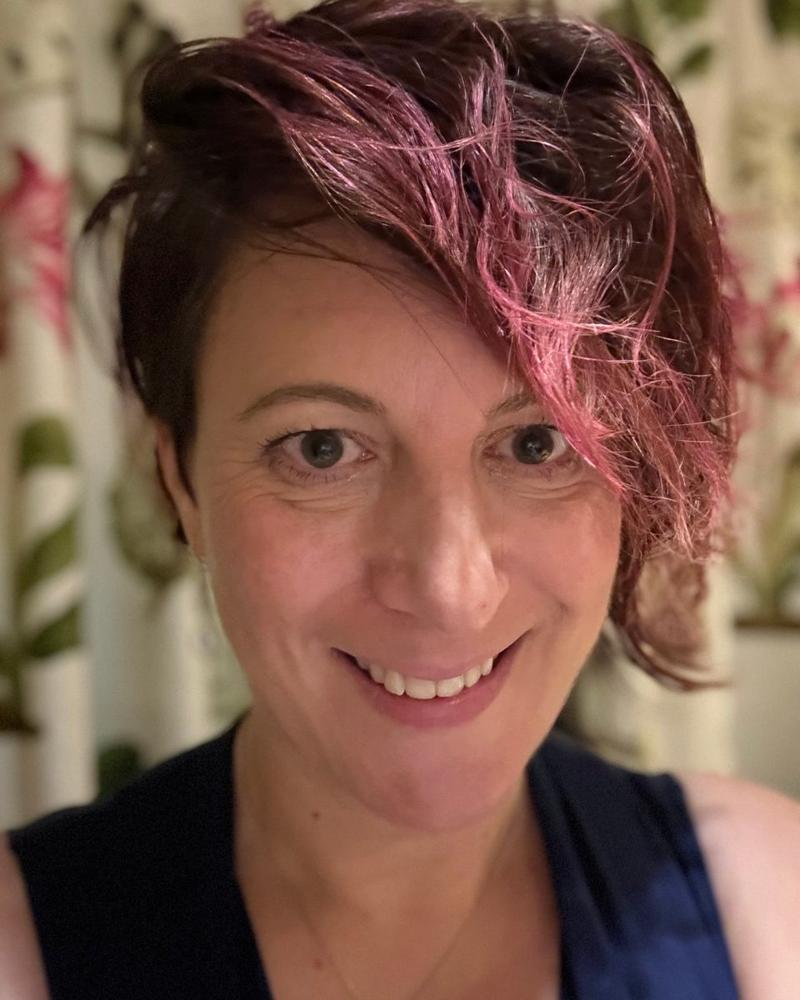 Emily Sas, smiling, with short dark hair and pink highlights